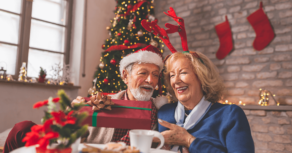 Elderly couple sitting by the Christmas tree exchanging gifts