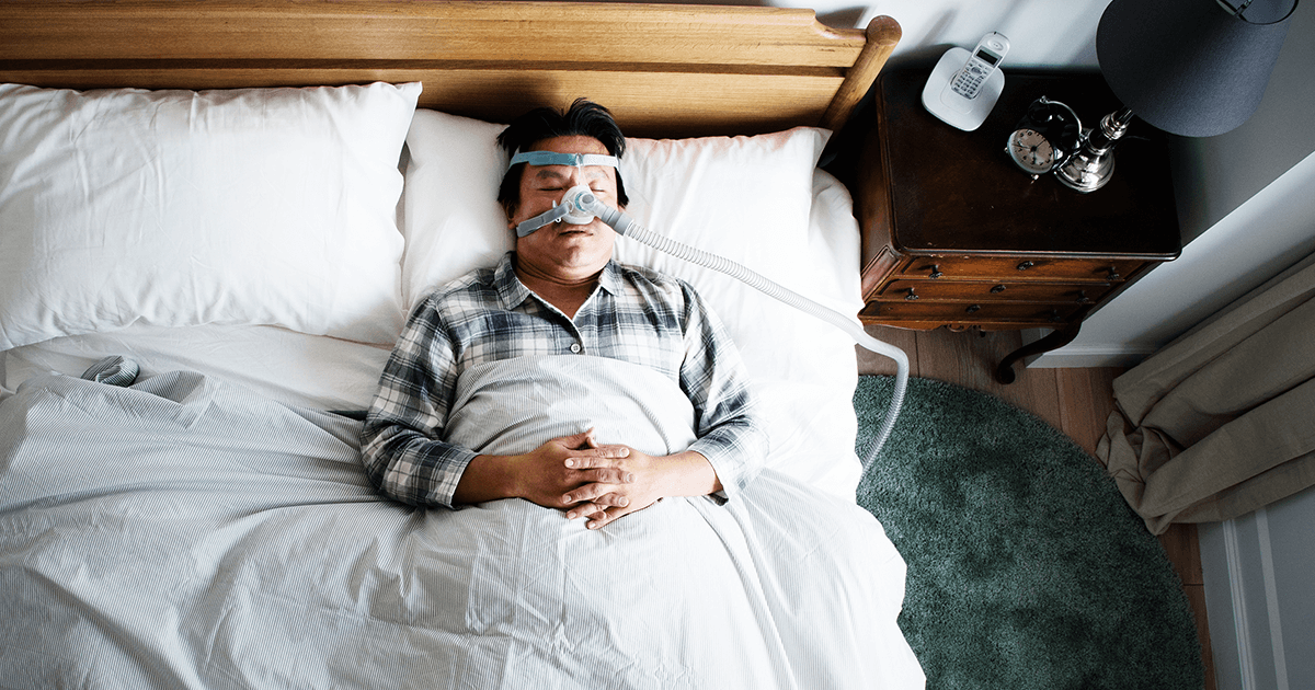 A man sleeping in a bed and managing sleep apnea with a CPAP machine 